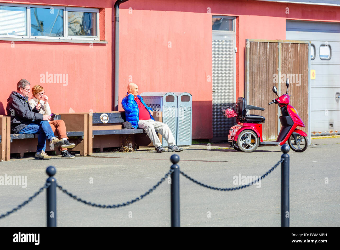 Simrishamn, Schweden - 1 April, 2016: Ältere Menschen und Paare sitzen Aalen in der Sonne diese warmen Frühlingstag. Geparkt elektrische wheelchai Stockfoto