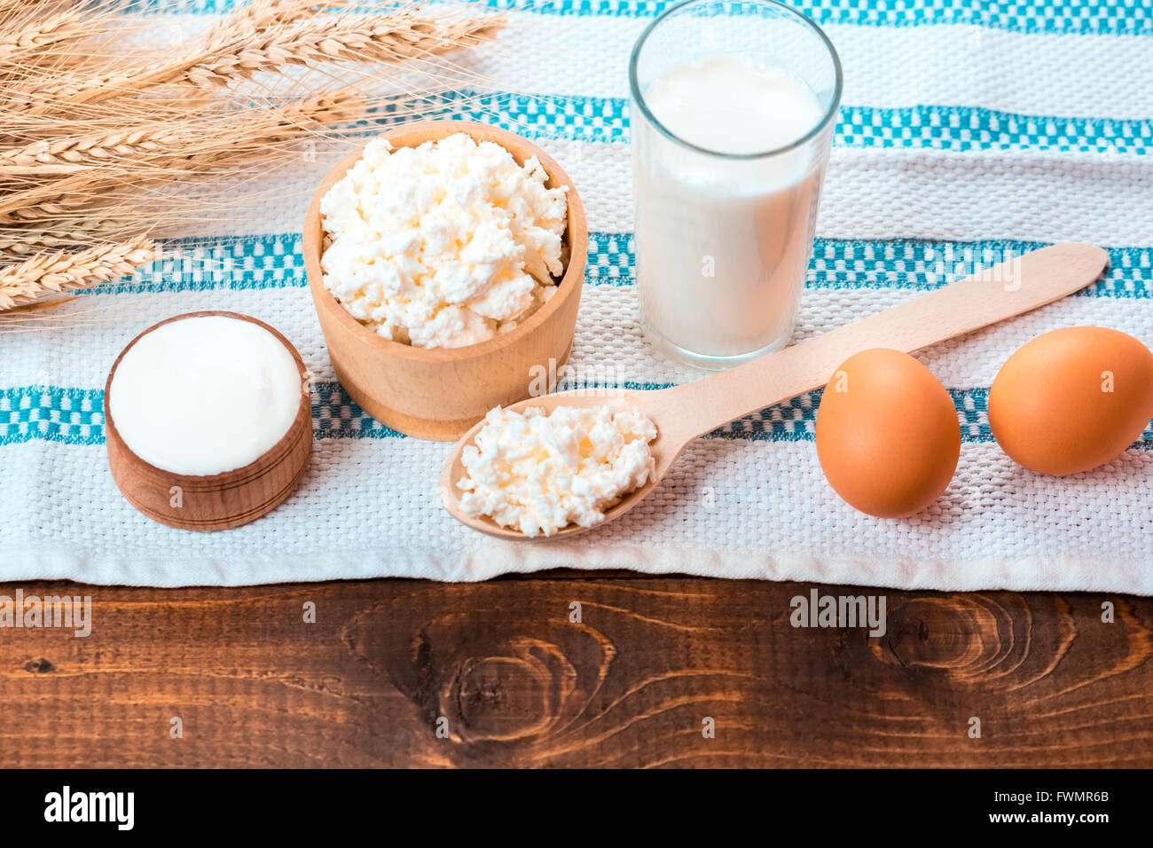 Hüttenkäse, Glas Milch, zwei Eier, Löffel aus Holz mit Quark und Weizen Ohren liegen auf der Serviette aus Sackleinen auf der Stockfoto