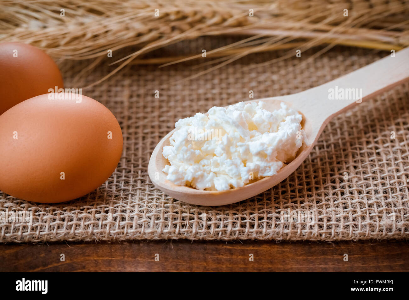 Zwei Eier, Löffel aus Holz mit Quark und Weizen Ohren liegen auf der Serviette aus Sackleinen auf dem alten Holztisch Stockfoto