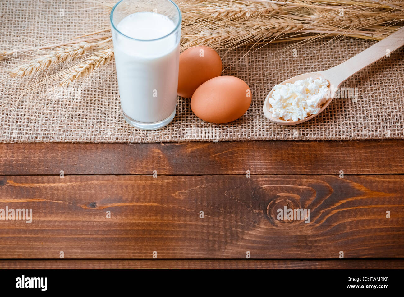 Zwei Eier, Löffel aus Holz mit Quark und Weizen Ohren liegen auf der Serviette aus Sackleinen auf dem alten Holztisch Stockfoto