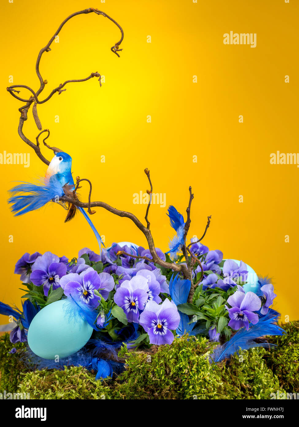 Ostern-Komposition mit blauen Vogel auf Ast sitzend mit violetten Blüten Ende blau Ei geschossen auf gelbem Hintergrund Stockfoto