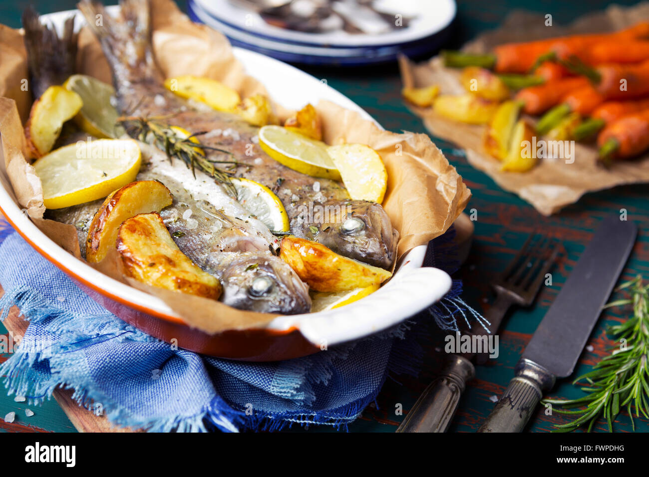 Ein Ofen gebratene Forellen in einem hohen Topf auf einem rustikalen Tisch. Mit Karotten und Kartoffeln auf der Seite. Stockfoto