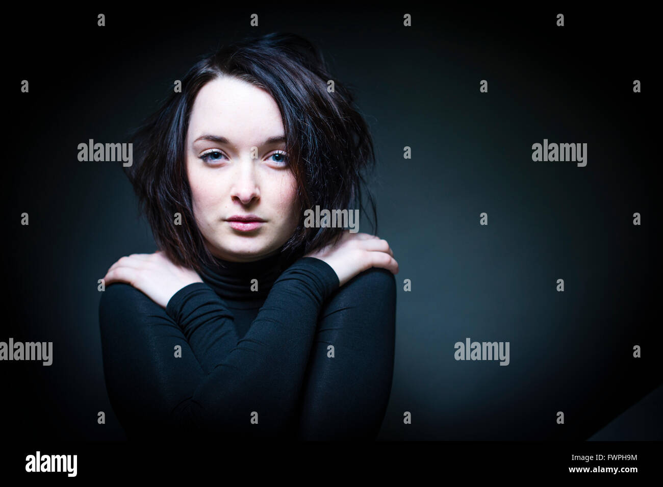 Ein junger Mensch, Frau, Mädchen, Teenager Anfang zwanzig, schlank, braune Haare, sucht zerzaust und allein und verletzlich, starren voraus, Arme gekreuzt Stockfoto