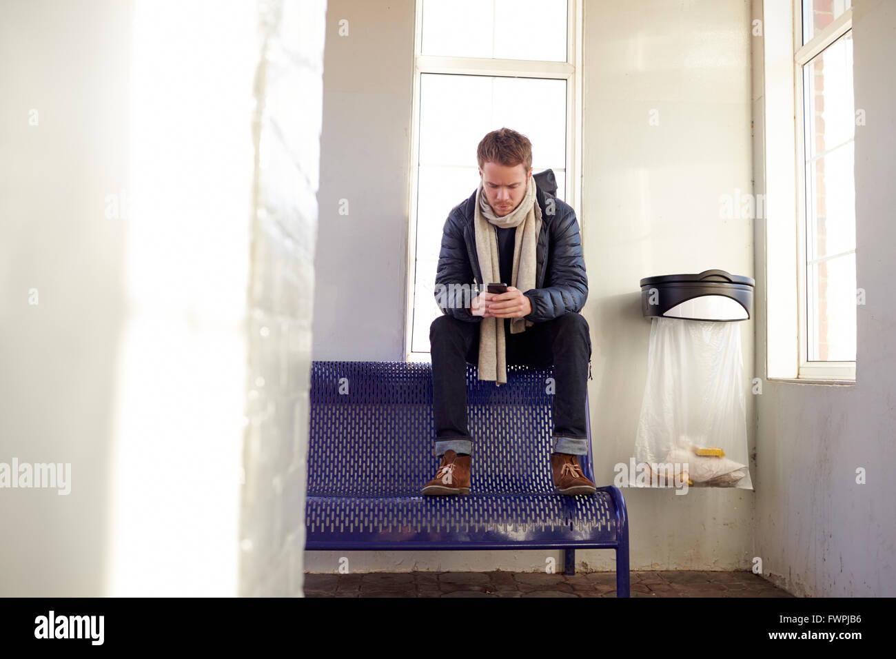 Mann sitzt auf Platz am Bahnhof SMS Stockfoto