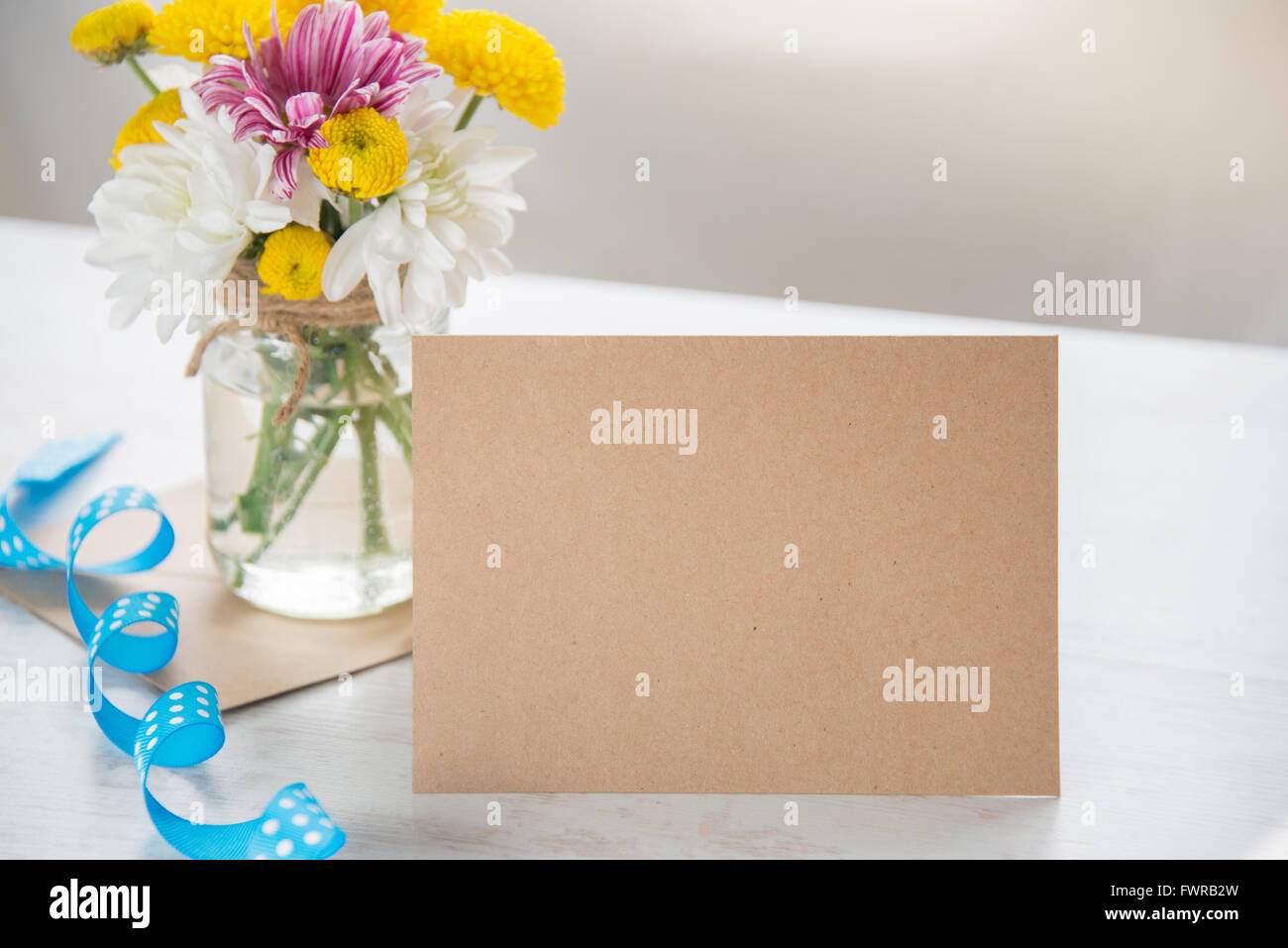 Frühling Blumen Blumenstrauß in einer Glas-Vase mit Kraft Karte Hinweis, Umschlag und blaue gepunktete Band auf weißem Holz rustikal Hintergrund Stockfoto