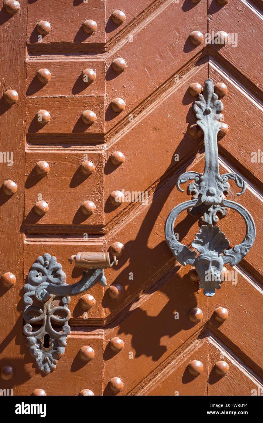 KUTNA HORA, Tschechien - 26. August 2015: Schmiedeeiserne Glocke und Griff auf orange Tür mit Metallnieten. Zentrale böhmische Stockfoto