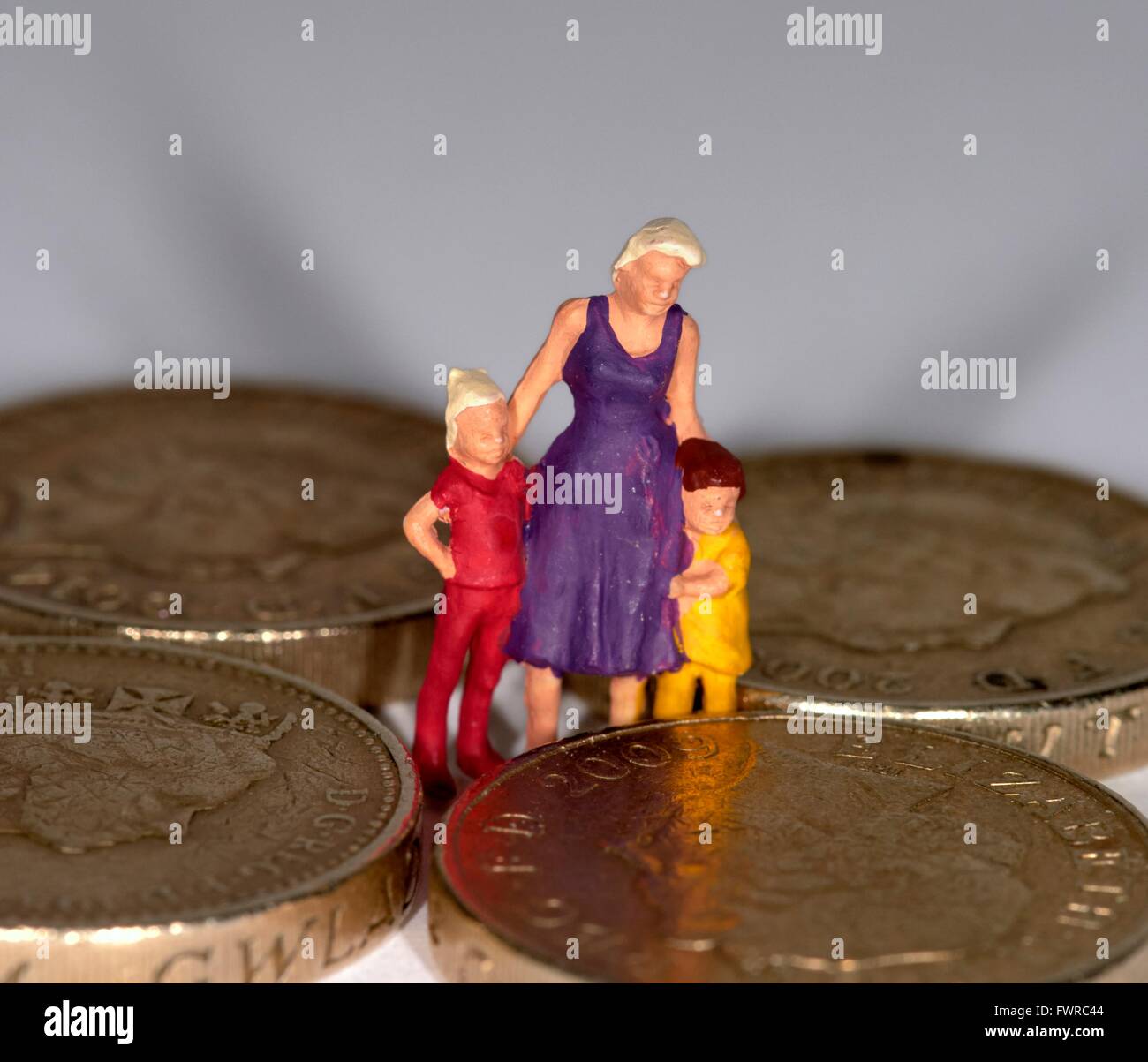 Eine Miniatur Figur Frau mit 2 Kindern steht zwischen einem Pfund-Münzen Stockfoto