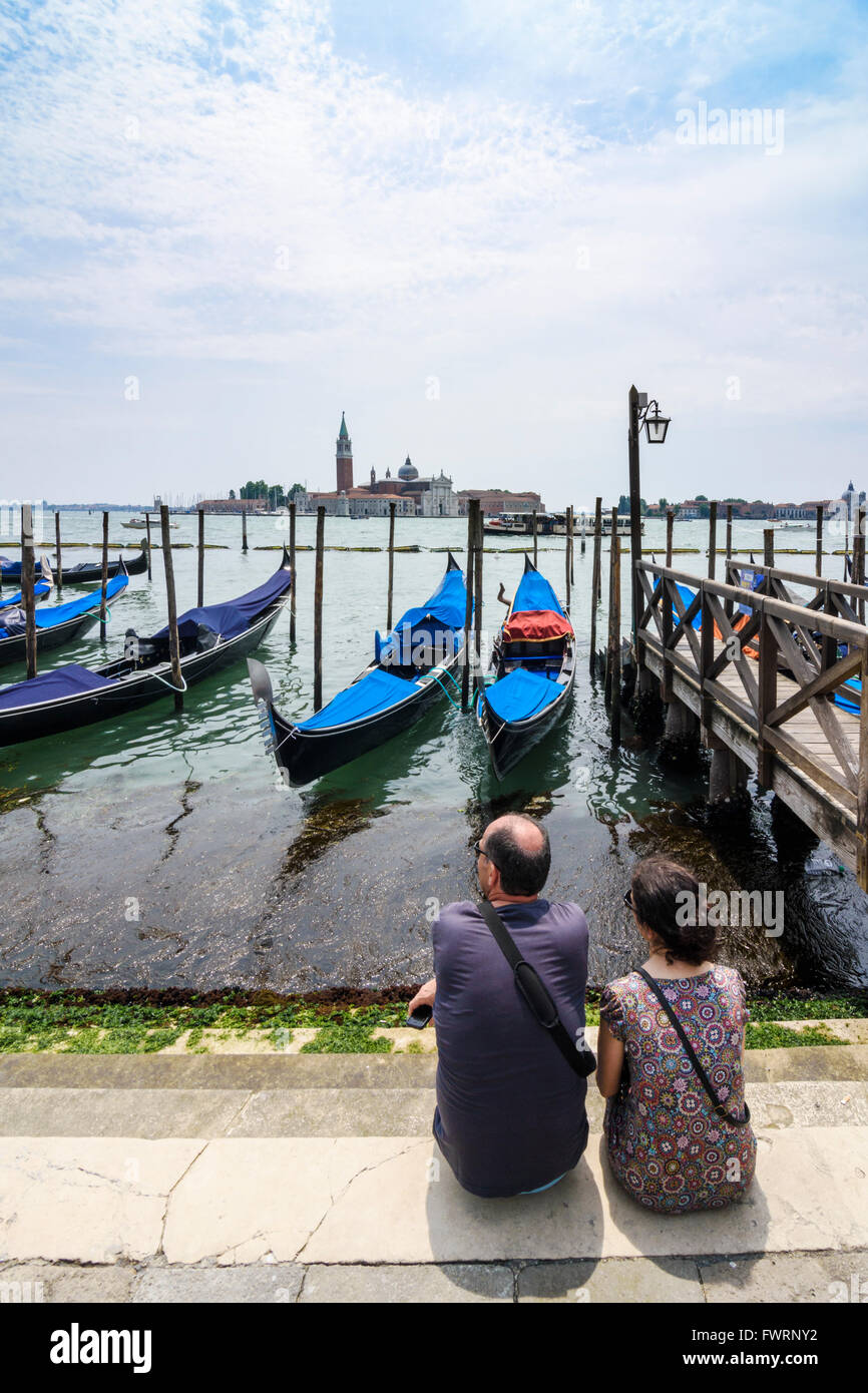 Ein paar genießen Sie den Blick über die festgemachten Gondeln in Richtung der Kirche von San Giorgio Maggiore, San Marco, Venedig, Italien Stockfoto