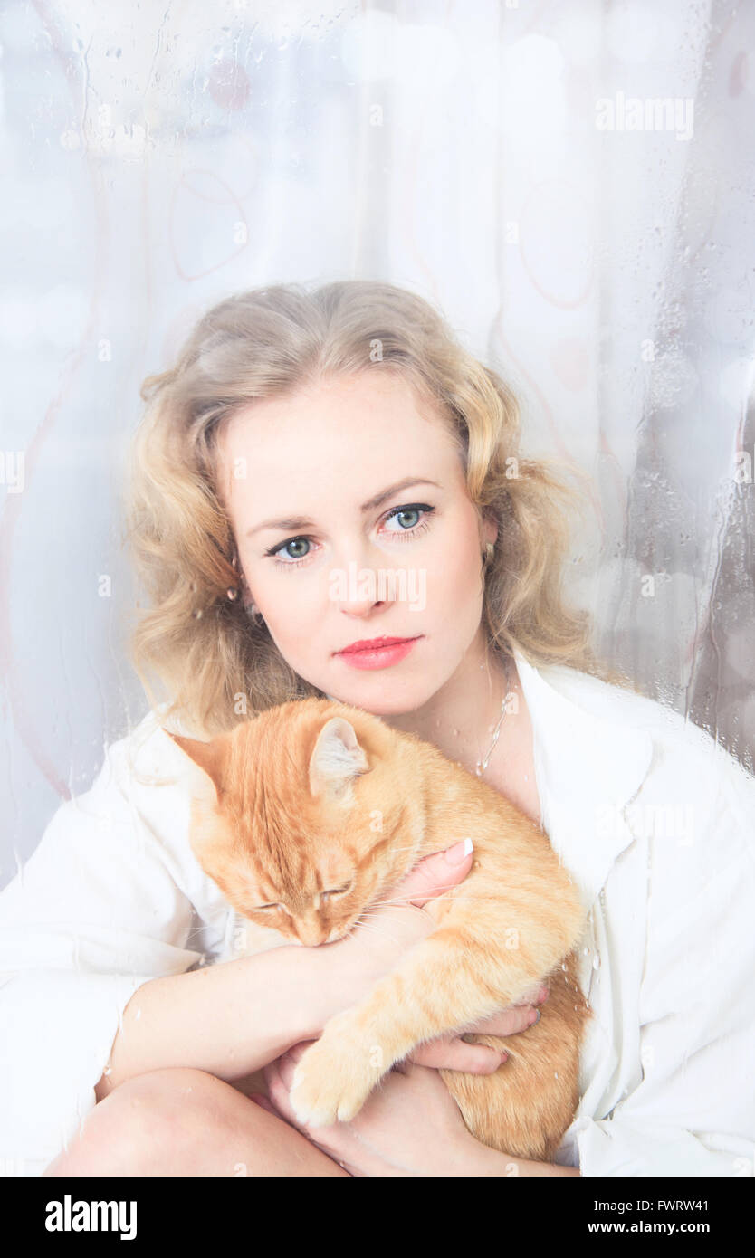 Schöne Frau am Fenster mit einer roten Katze an ihren Händen Stockfoto