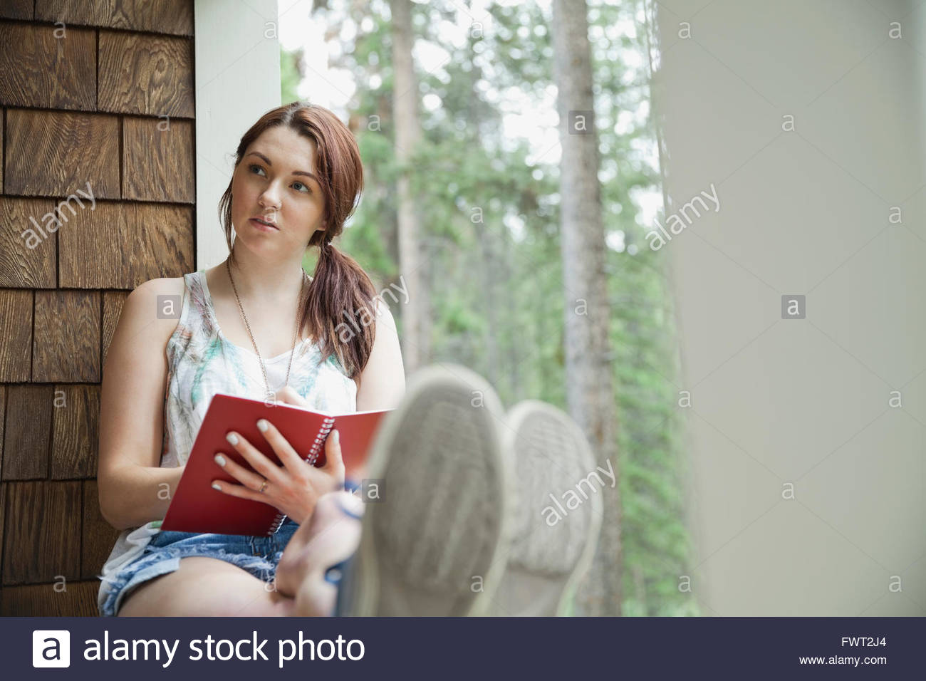 Nachdenkliche Frau sitzt auf Kabine Veranda mit journal Stockfoto