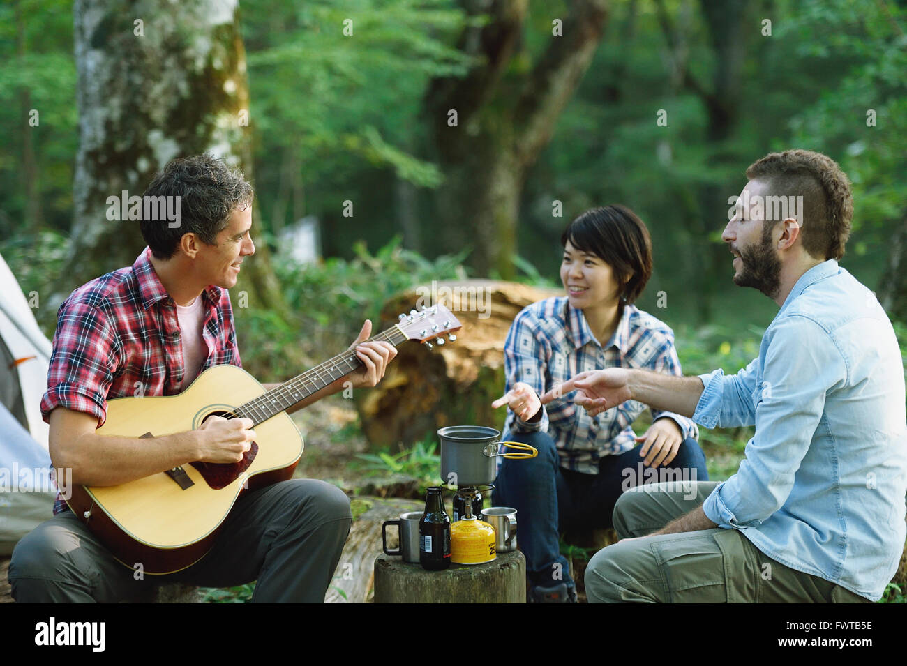 Multi-ethnischen Gruppe von Freunden, die Gitarre zu spielen, auf einem Campingplatz Stockfoto