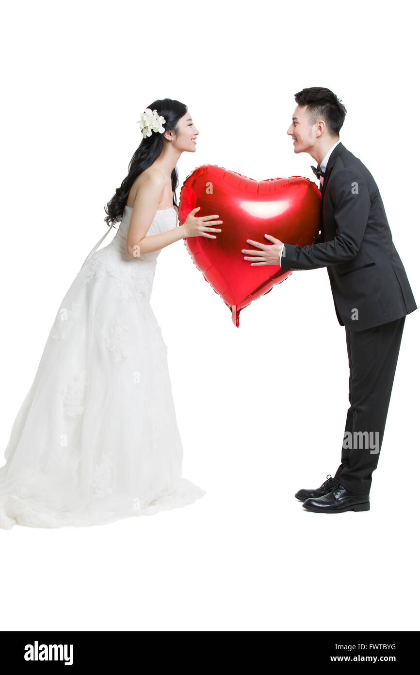 Glückliche Braut und Bräutigam halten einen herzförmigen Ballon Stockfoto