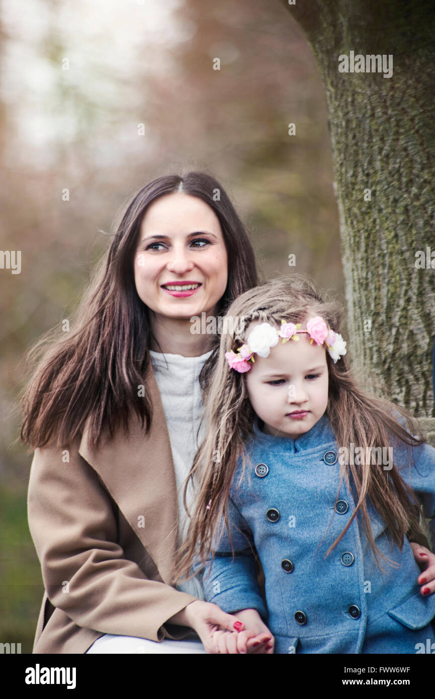 junge Frau mit ihrer kleinen Tochter unter dem Baum sitzt Stockfoto