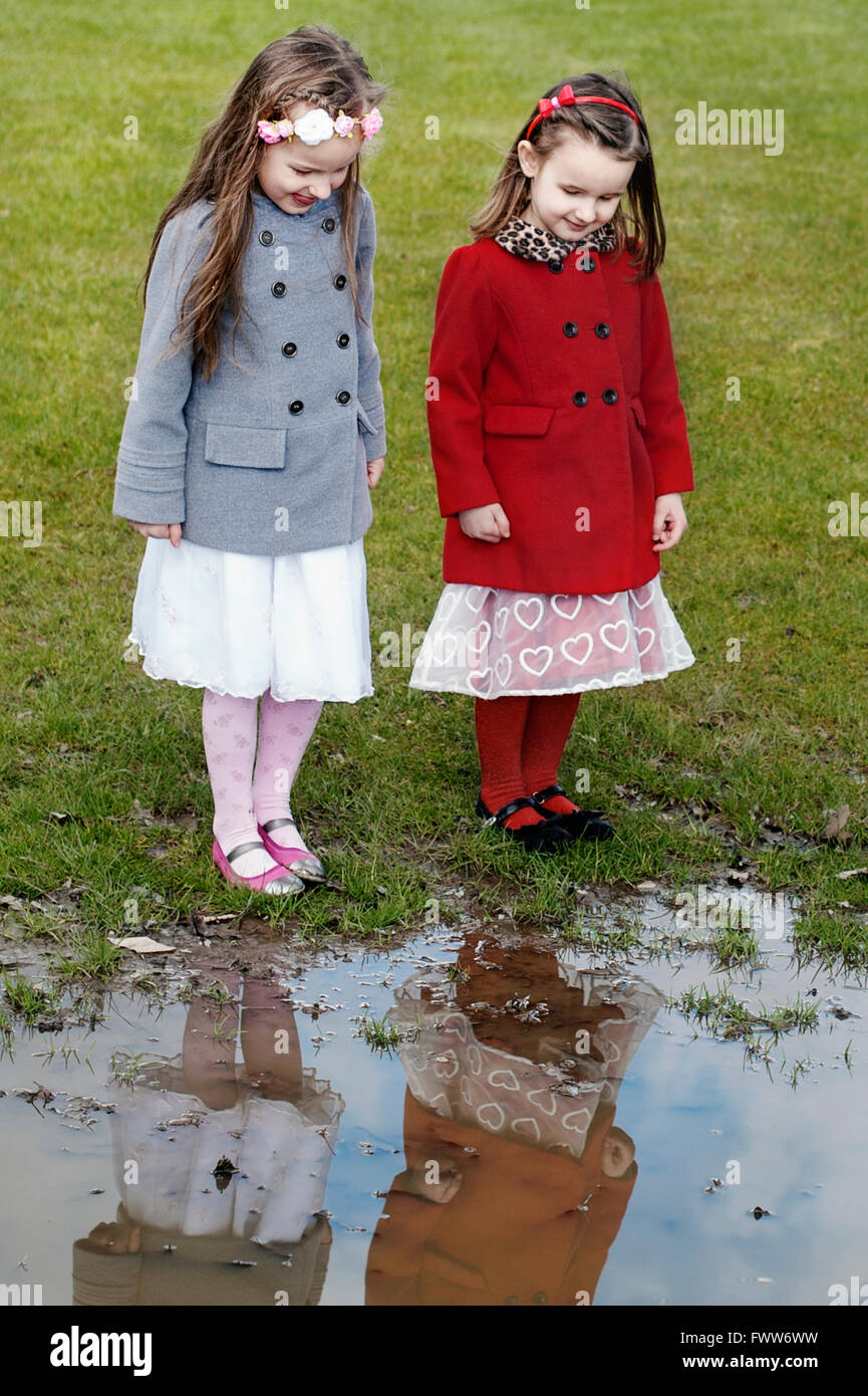 zwei kleine Schwestern stehen durch die Pfütze Wasserreflexion betrachten Stockfoto