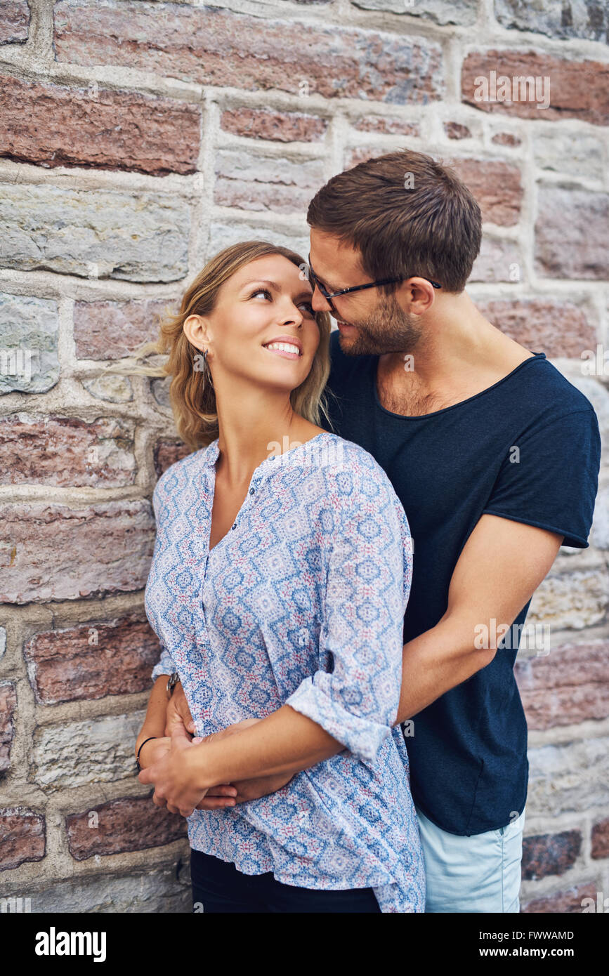 Die Hälfte Körper geschossen von einem Mann umarmt seine Frau hinter Romantisch und Lächeln Einander gegen Mauer Hintergrund. Stockfoto