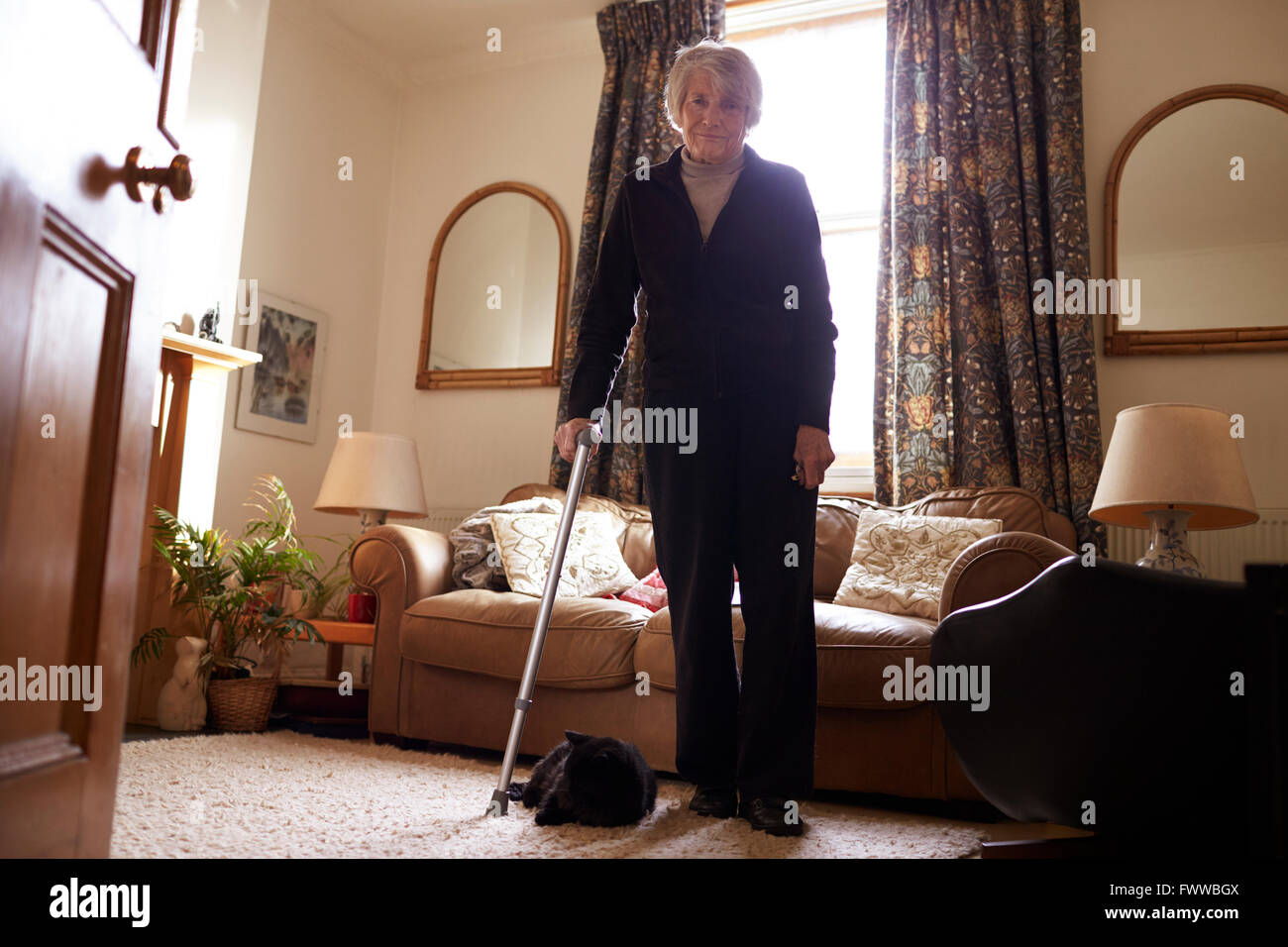 Portrait von Senior Frau mit Krücke stehen In der Lounge Stockfoto