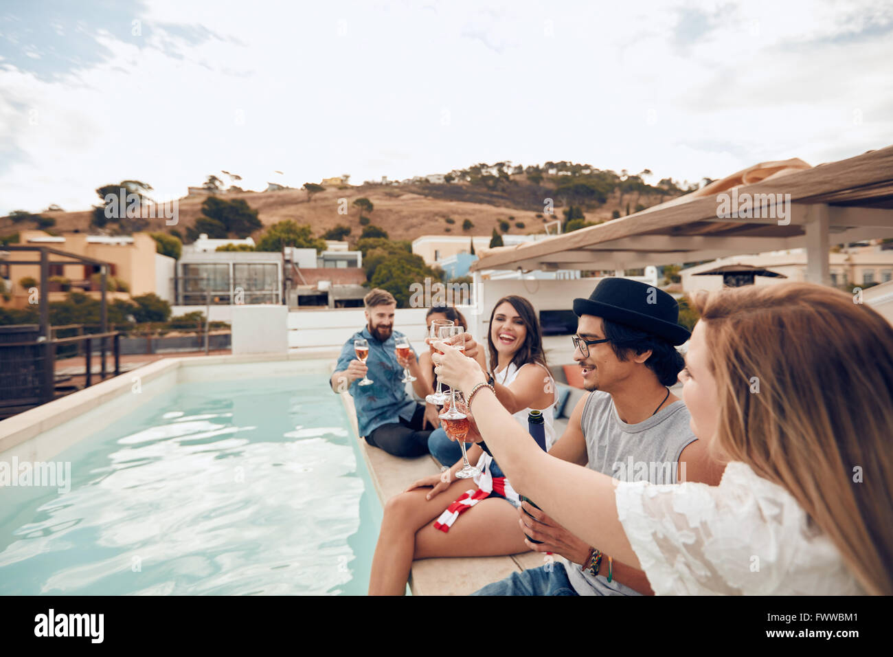 Im Freien Schuss glücklich junger Menschen sitzen auf dem Rand des Pools mit einer festlichen Toast. Freunde heben einen Toast während einer Stockfoto