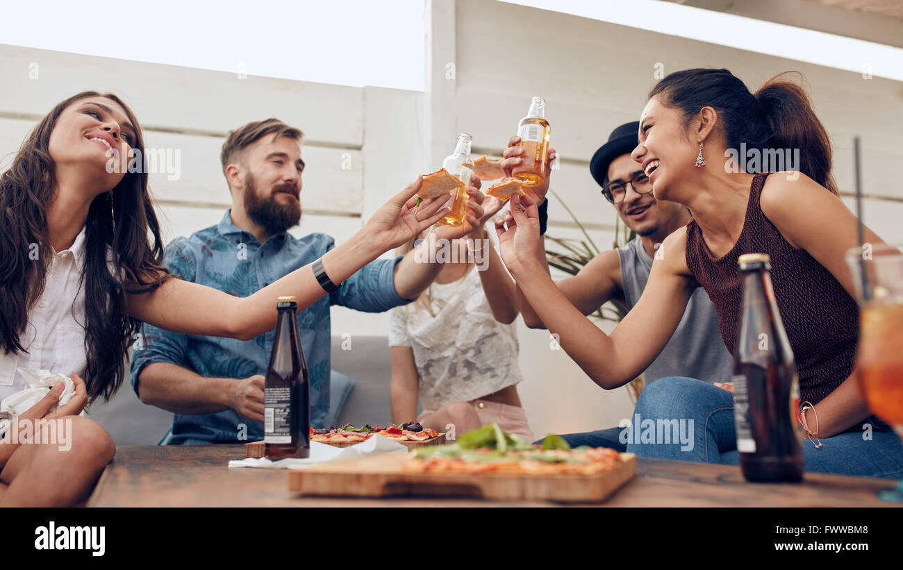 Gruppe von Freunden Toasten Biere in einer Partei beim Tisch sitzen. Gemischtrassig Freunde hängen auf der Dachterrasse genießen Sie Partei Stockfoto