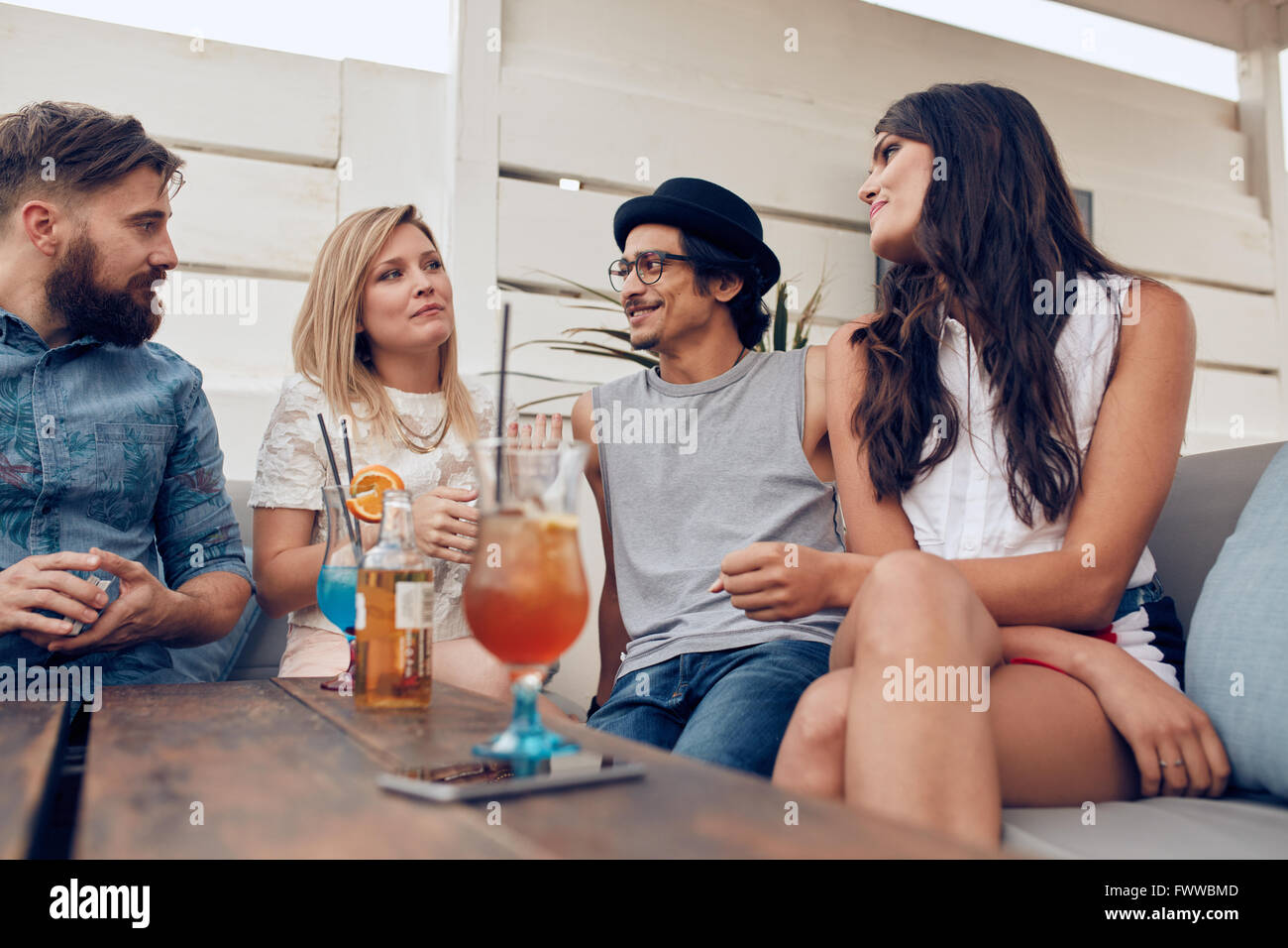 Gruppe junger Menschen sitzen um einen Tisch im Chat. Junge Freunde zusammen feiern, mit Cocktails am Tisch. Stockfoto
