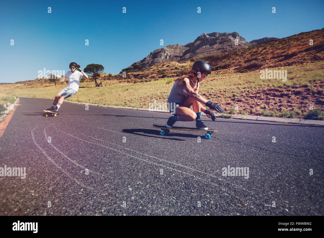 Zwei junge Menschen, die lange üben an Bord Reiten im Freien auf der Landstraße. Mann und Frau Longboarding an einem Sommertag. Stockfoto