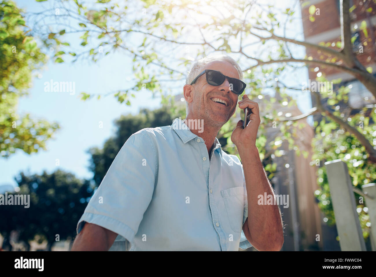 Porträt von glücklich reifer Mann telefonieren mit Handy im Freien in der Stadt an einem sonnigen Tag. Senior kaukasischen Mann Anruf tätigen Stockfoto