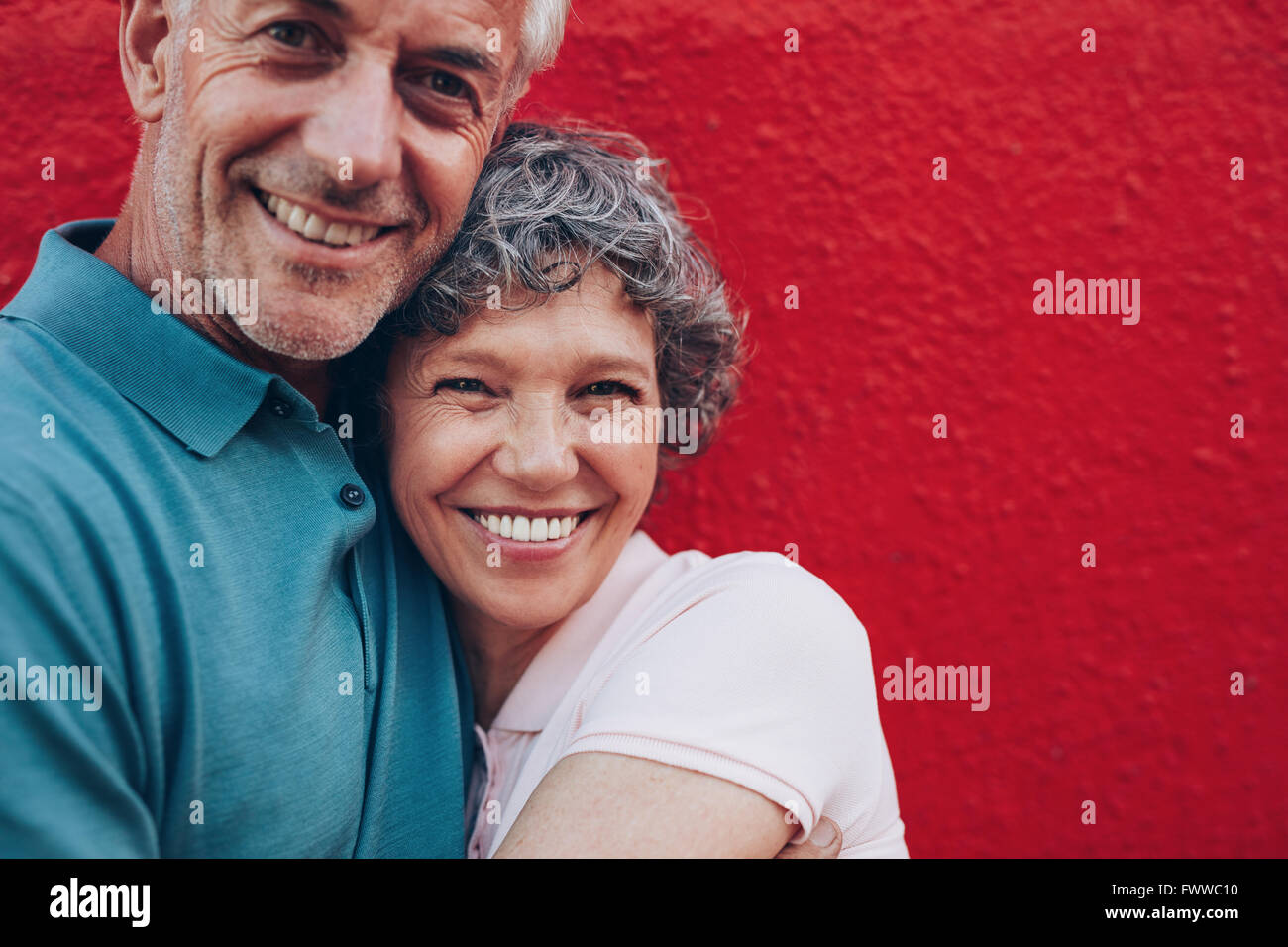 Porträt von fröhlichen mittleren gealterten paar umarmen einander vor rotem Hintergrund. Ältere Mann und Frau gemeinsam gegen rot w Stockfoto