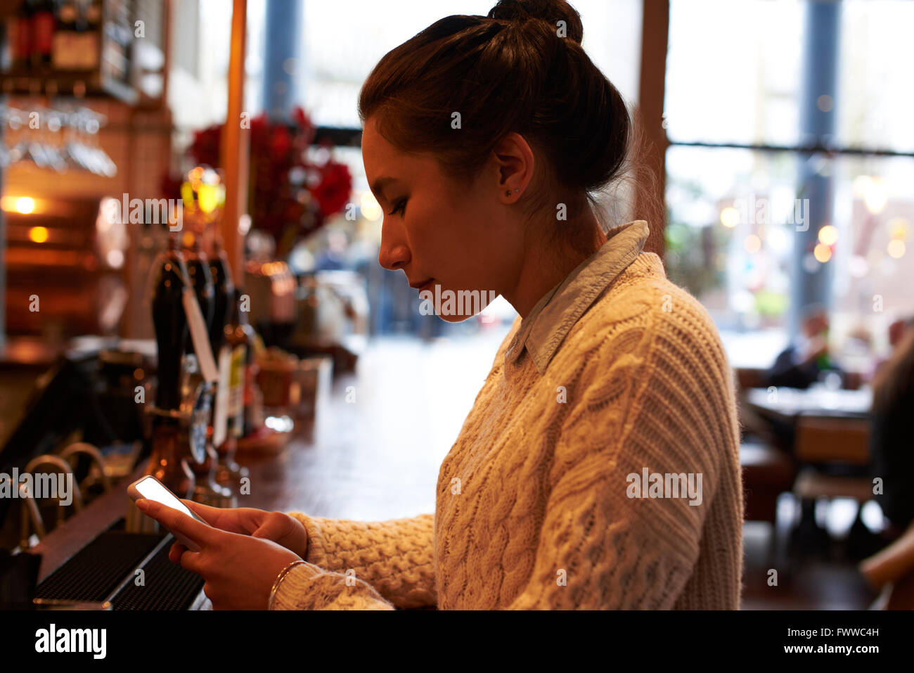 Junge Frau sitzt Bar SMS Stockfoto