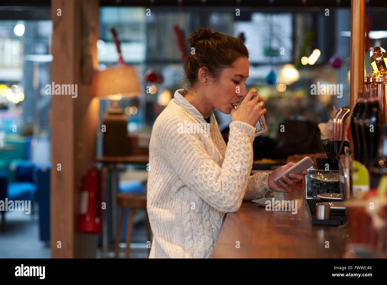 Junge Frau sitzt Bar SMS Stockfoto