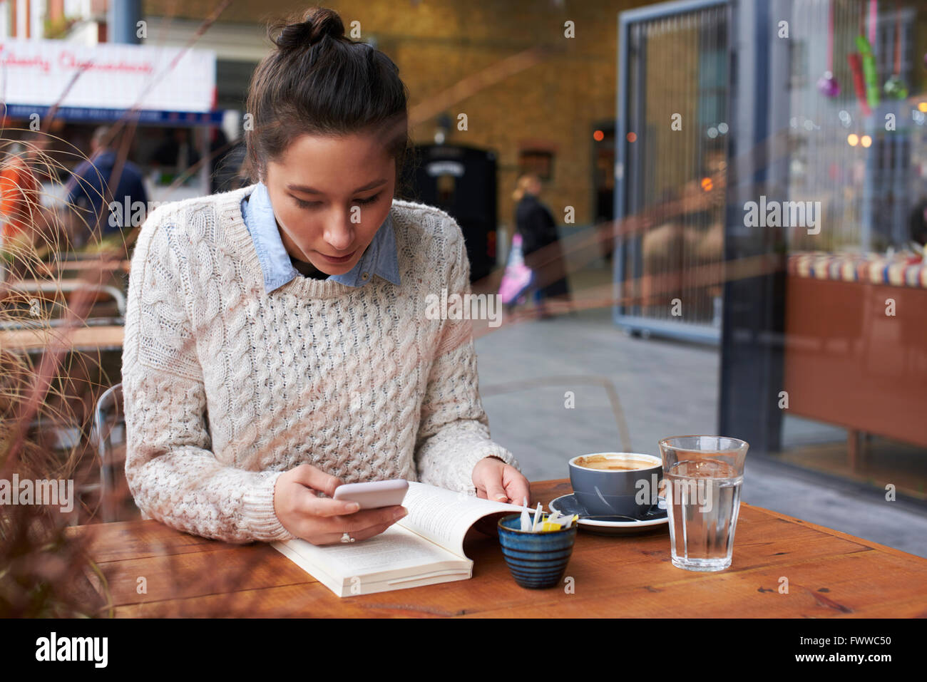 Junge Frau Lesebuch und Textnachrichten In Coffee-Shop Stockfoto