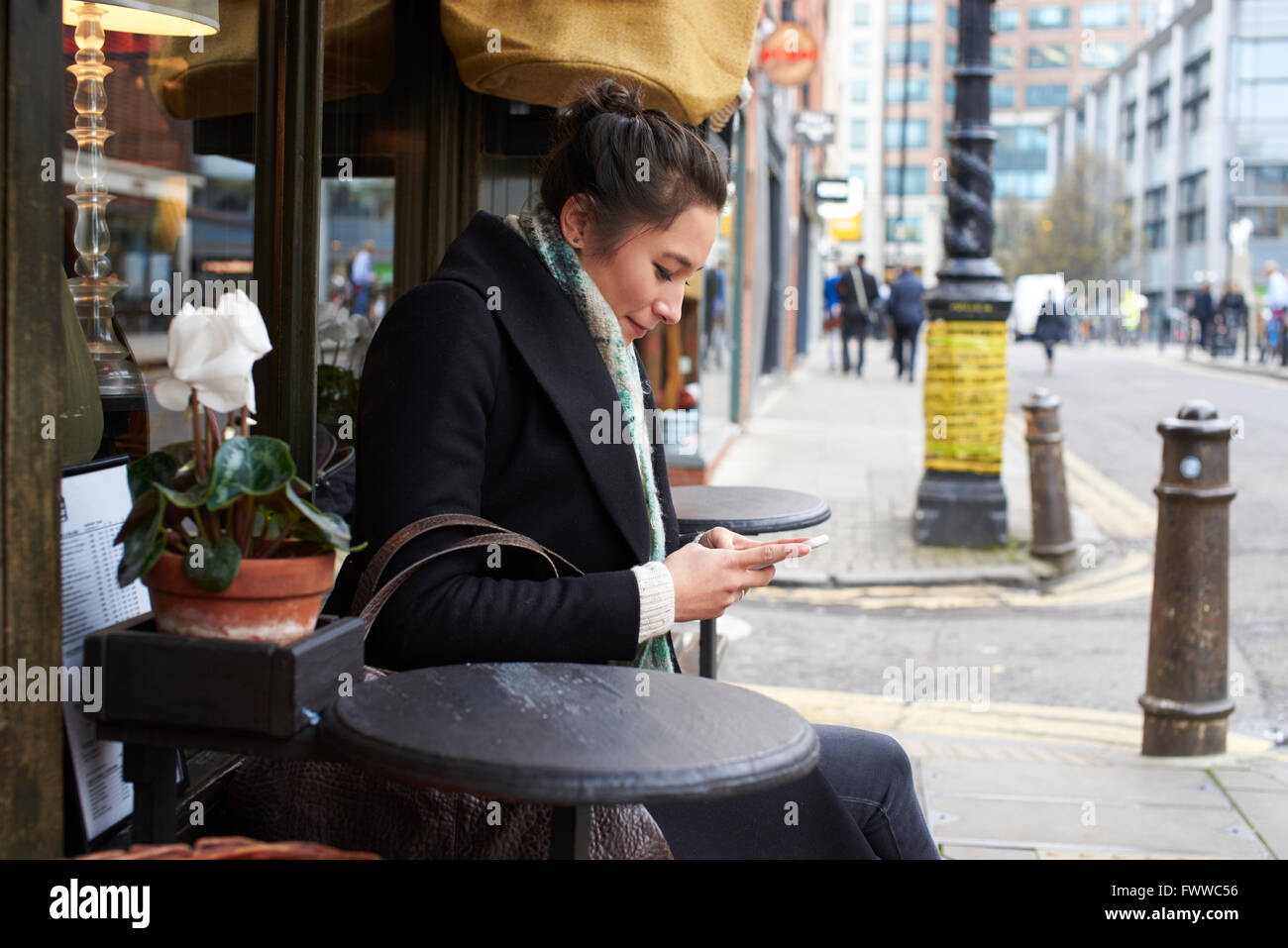 Junge Frau sitzt außen Café lesen SMS Stockfoto