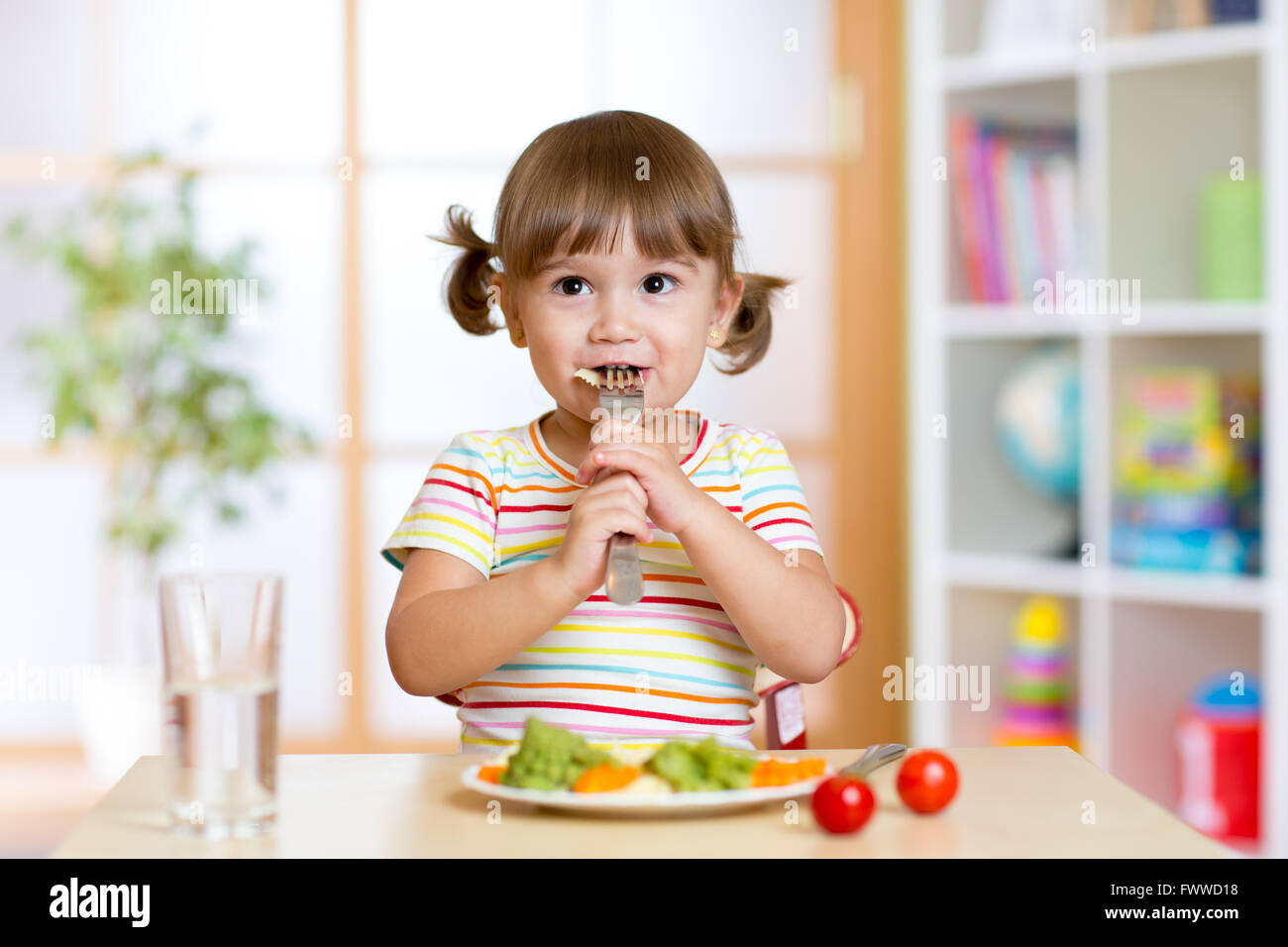Kleines Mädchen untersucht Rosenkohl. Kind mit gesunden Lebensmitteln, die am Tisch im Kindergarten Stockfoto