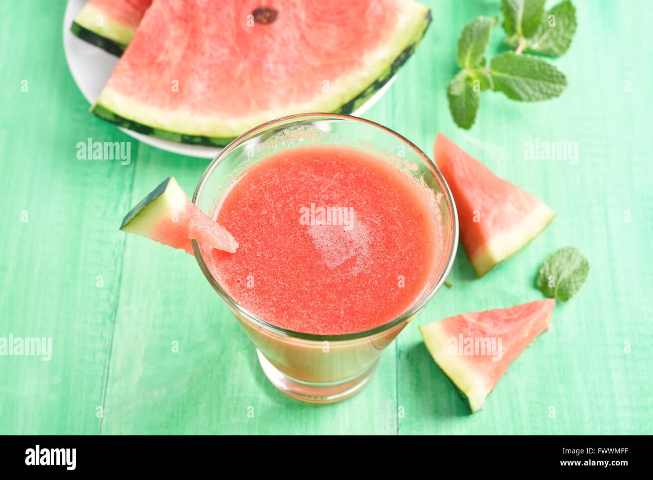 Wassermelonensaft im Glas und Scheiben auf grünem Hintergrund aus Holz Stockfoto