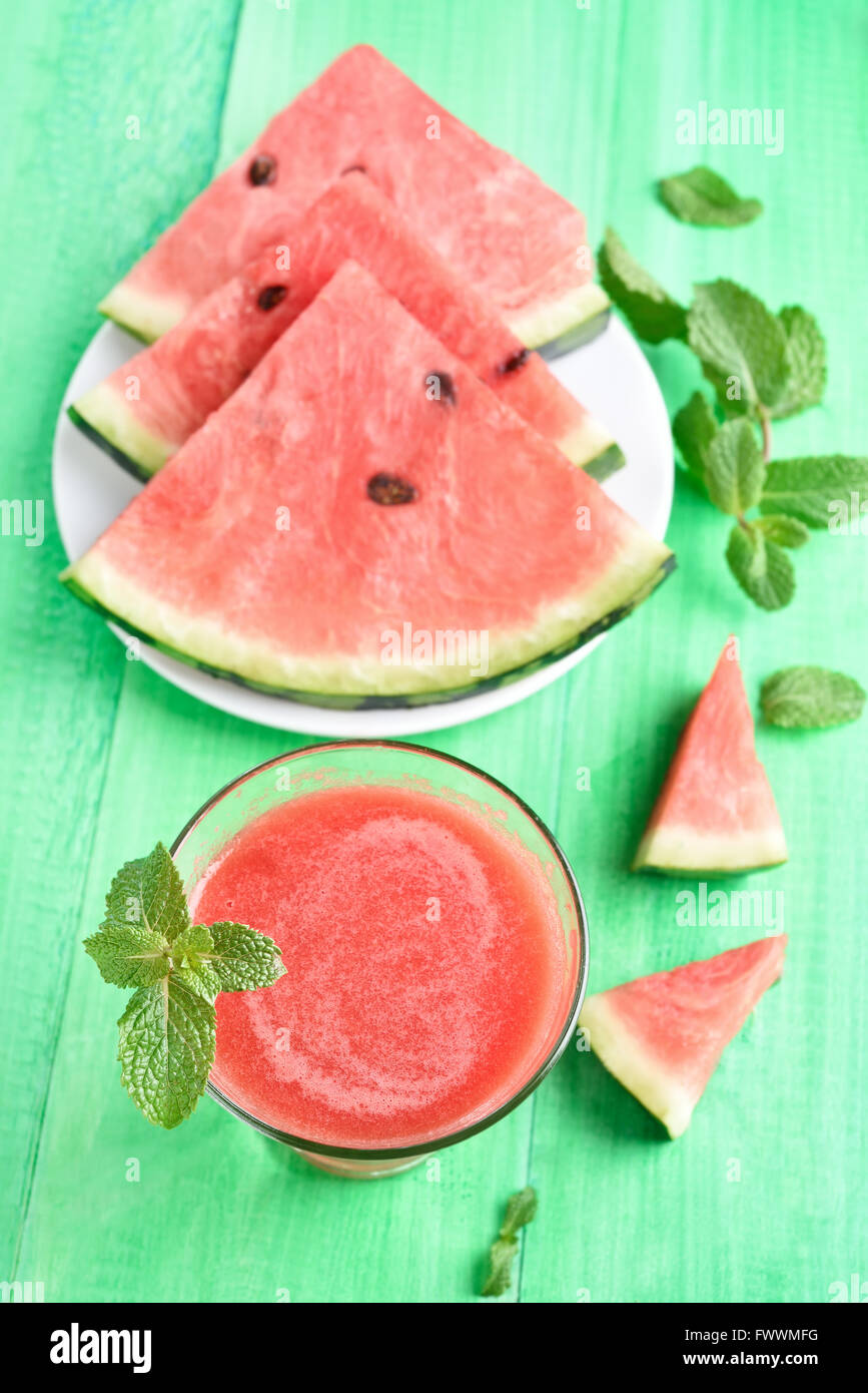 Wassermelonen-Smoothie in Glas und Scheiben auf grünen hölzernen Hintergrund, Ansicht von oben Stockfoto