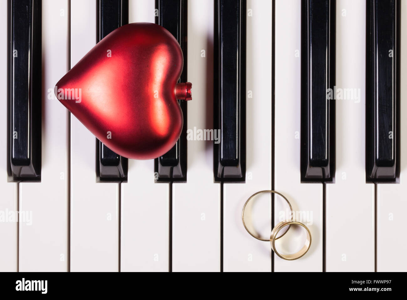 Detail der Klaviertastatur, rotes Herz und Trauringe Stockfoto