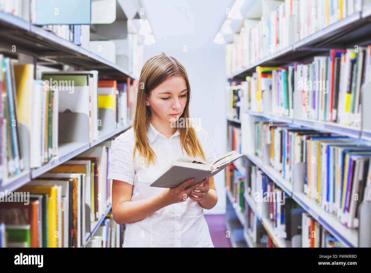junges Mädchen Student Lesebuch zwischen den Regalen in der Bibliothek Stockfoto