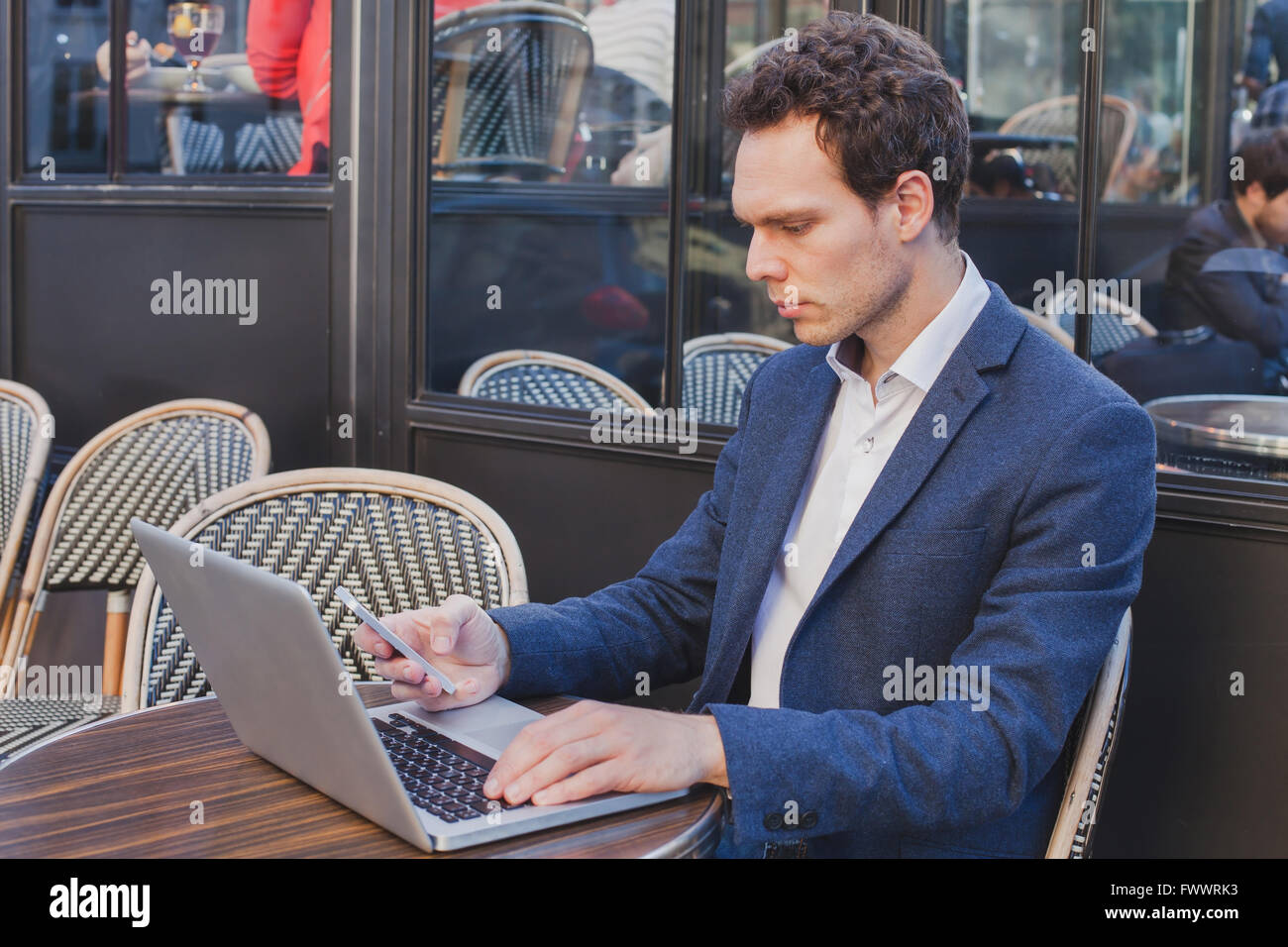 junge hübsche Buisnessman mit Internet auf Handy während der Sitzung in offenen Straßencafé Stockfoto
