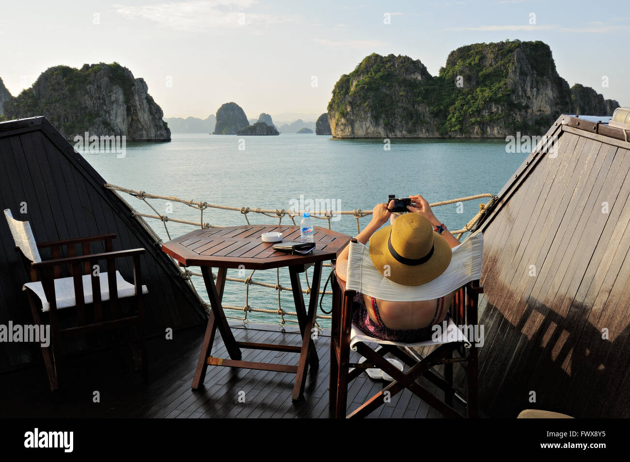 Kaukasische Mädchen auf einem Stuhl sitzend nimmt ein Bild auf Bai Tu Long Gebiet der Ha Long Bay vom Deck einer Dschunke, Vietnam Stockfoto