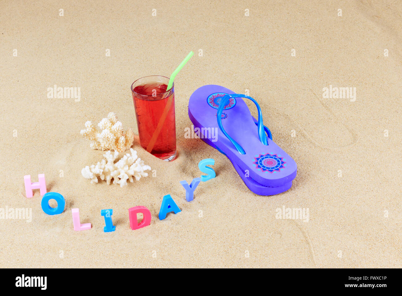 Paar blau Flip flops mit Korallen, Frucht trinken aus Glas mit Stroh und farbigen Buchstaben Rechtschreibung Ferien auf einem sand Stockfoto