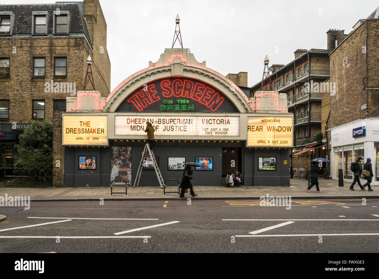Ein Mann auf einer Leiter korrigiert die Rechtschreibung auf der Vorderseite des Bildschirms auf die grüne Kino am Upper Street, Islington, London, UK Stockfoto