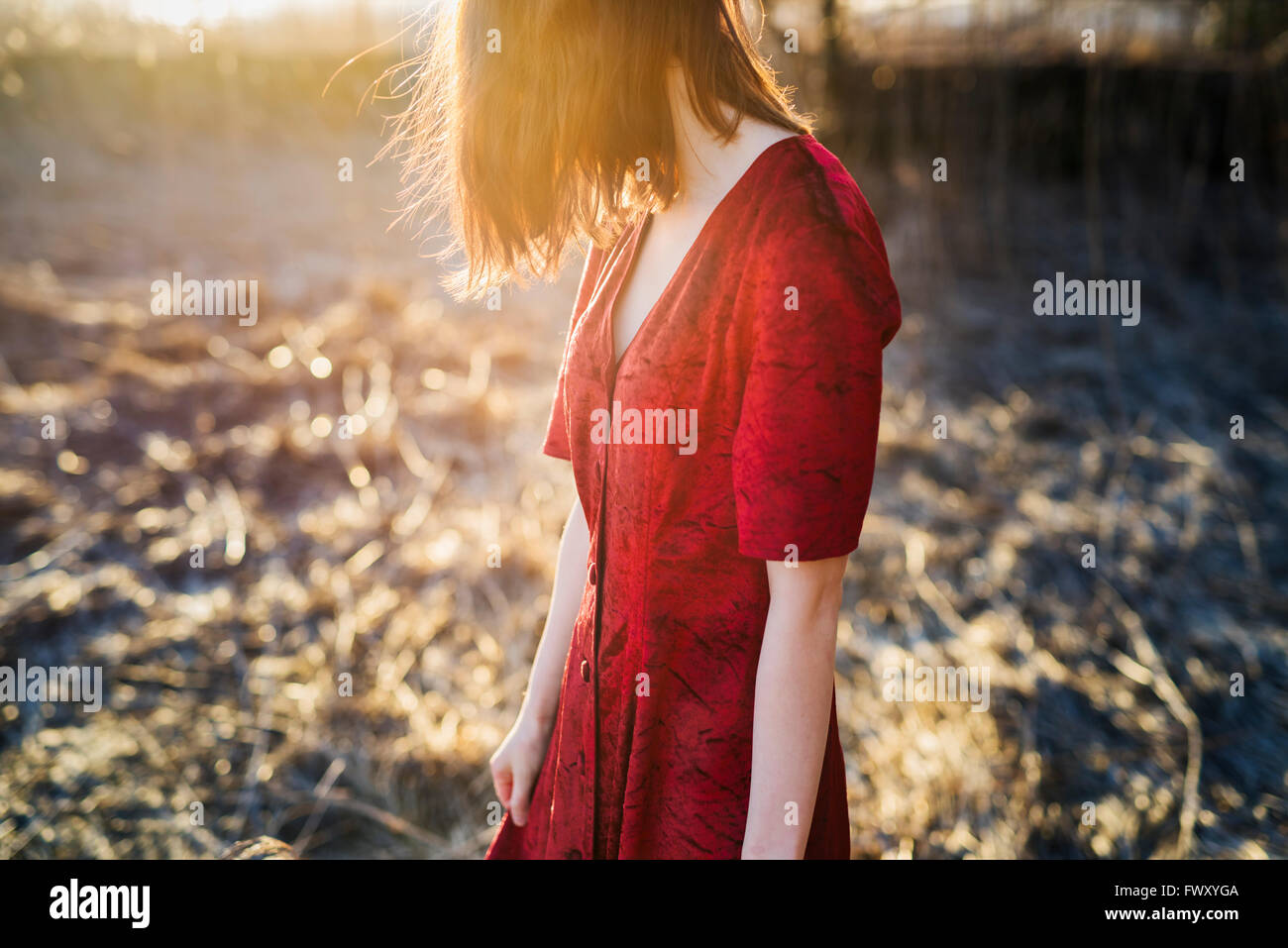 Finnland, Varsinais-Suomi, junge rote Haare Frau im roten Kleid stehen im Sonnenlicht Stockfoto