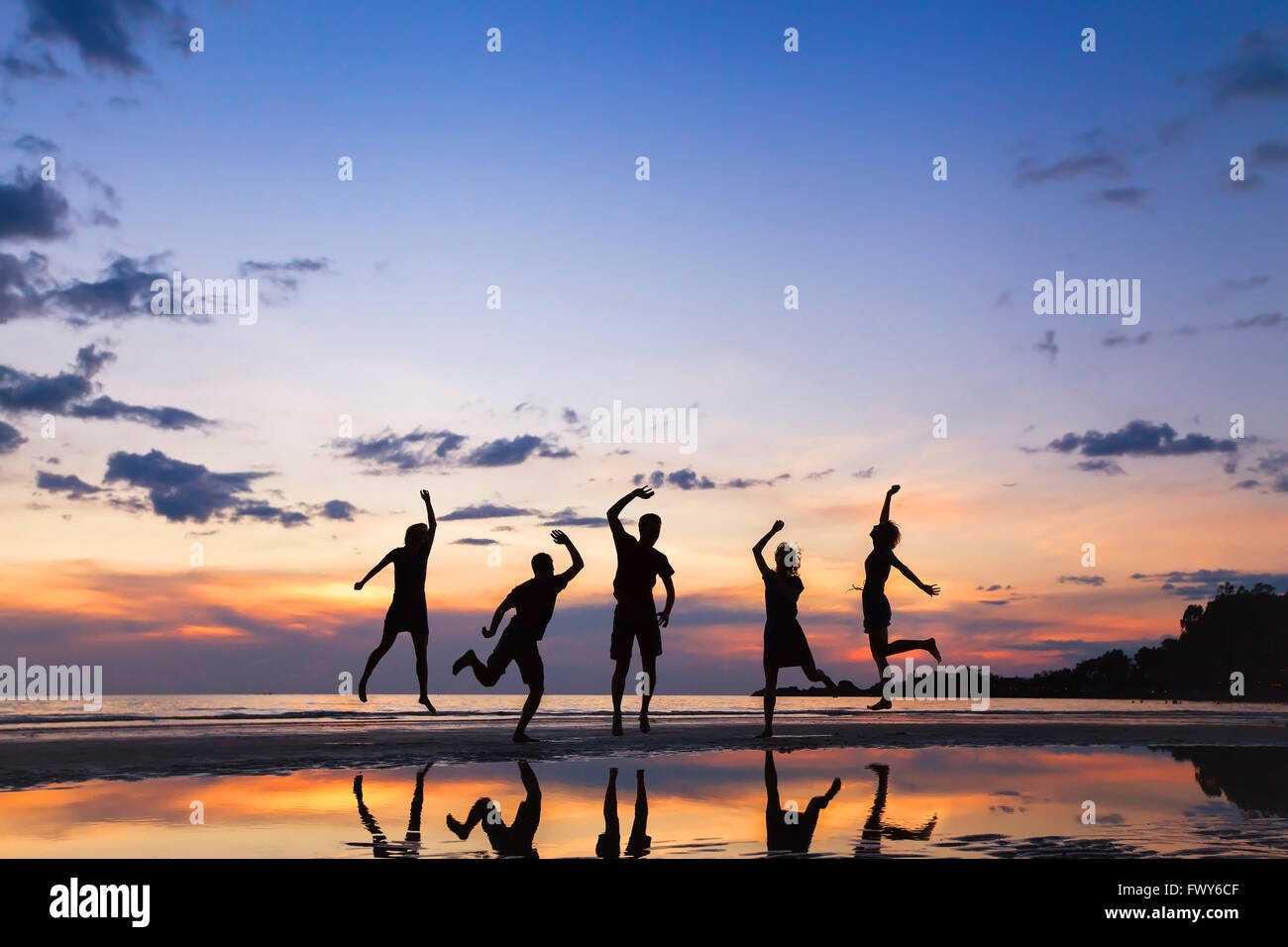 Gruppe von Menschen springen am Strand bei Sonnenuntergang, Silhouette von Freunden gemeinsam Spaß haben Stockfoto