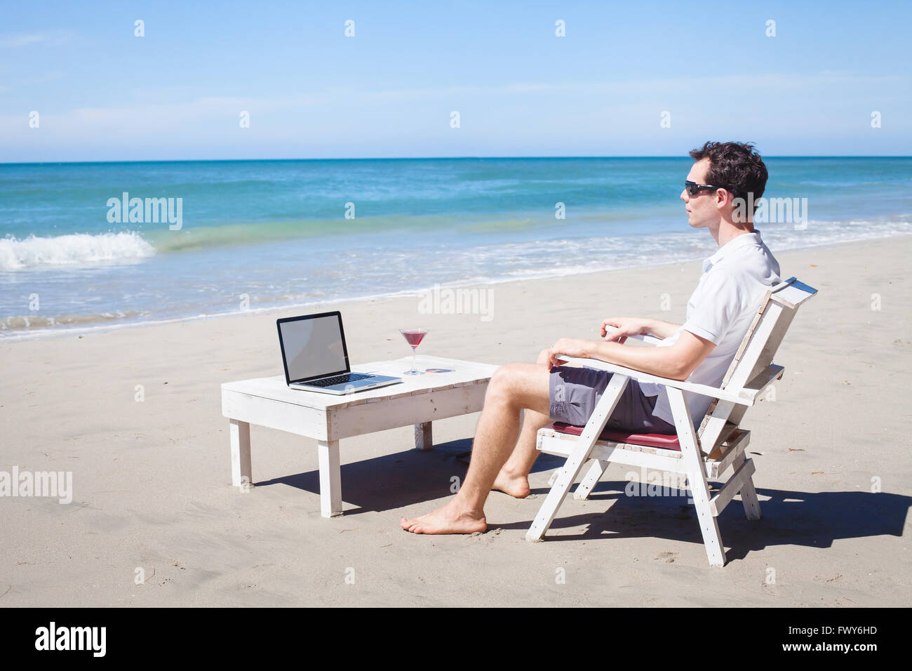 Telearbeit, Geschäftsmann, entspannen am Strand mit Laptop und cocktail, freier Mitarbeiter am Arbeitsplatz, Traumjob Stockfoto