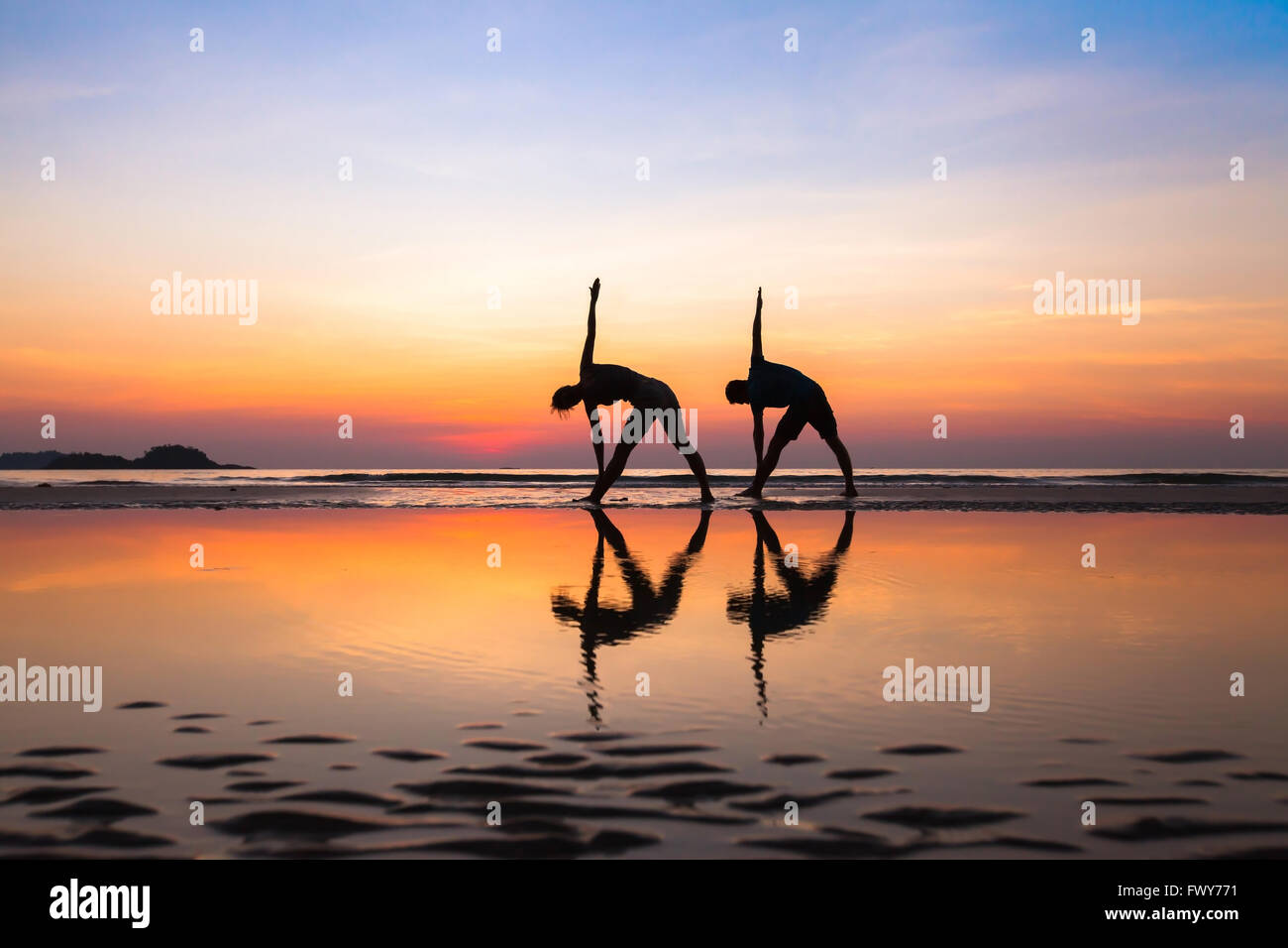 Strecken am Strand bei Sonnenuntergang, Yoga-Übungen, Silhouetten von paar Stockfoto
