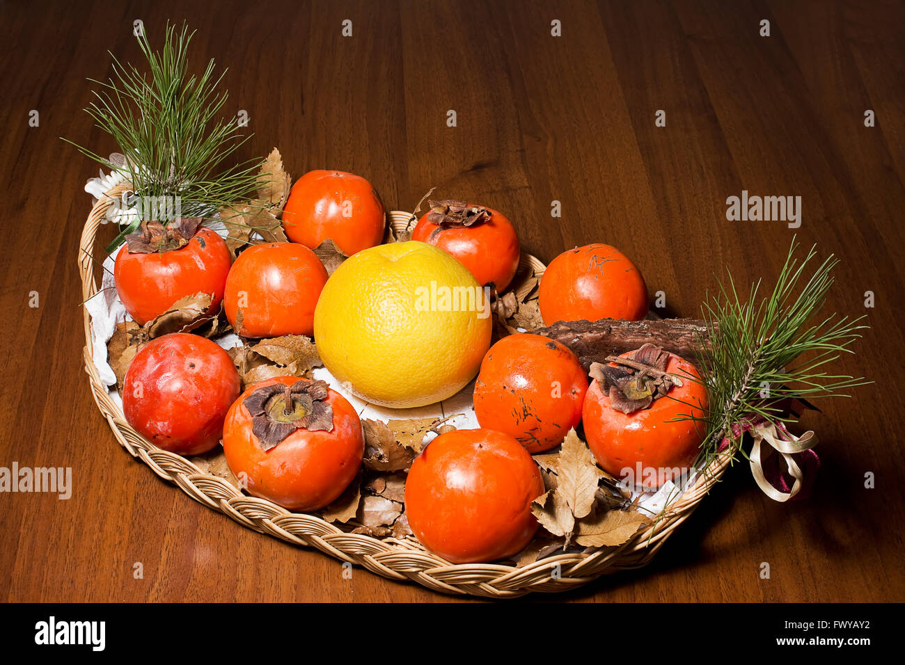 Zusammensetzung der Kaki, Grapefruit und Kiefer Kegel in die Schale auf den Tisch Stockfoto