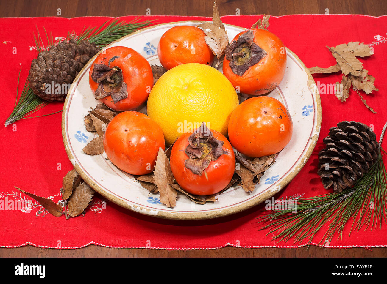 Zusammensetzung der Kaki, Grapefruit und Kiefer Kegel in die Schale auf den Tisch Stockfoto