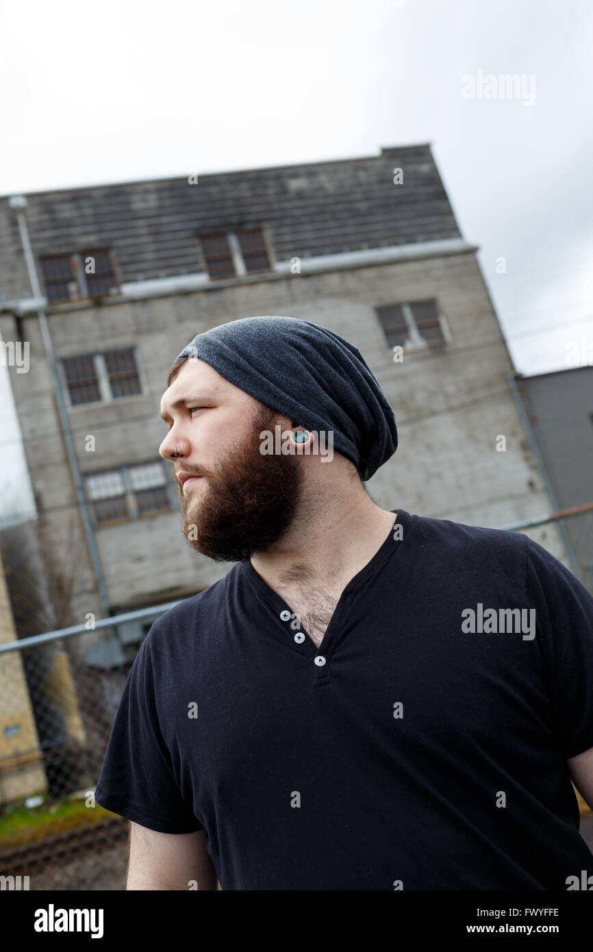 Junger Erwachsener Mann im Freien in einem städtischen Umfeld für Lifestyle Portrait eines bärtigen Hipster. Stockfoto