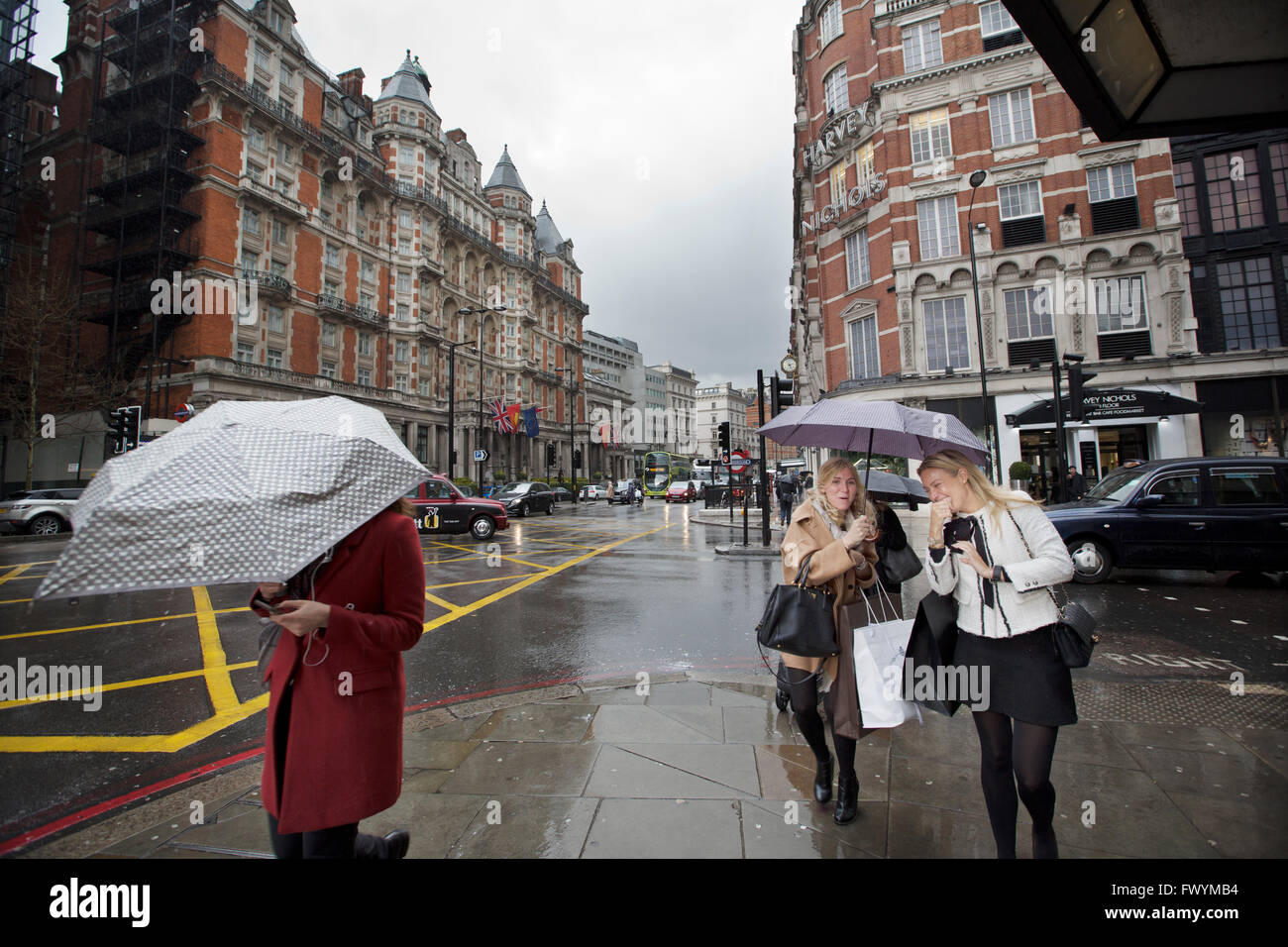 Junge Frauen auf eine shopping Reise in Knightsbridge Zuflucht vor dem Regen unter Sonnenschirmen, überqueren die Straße, London, UK Stockfoto