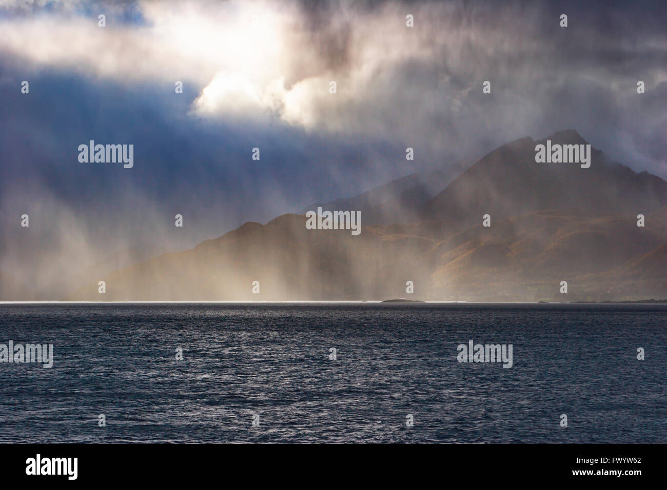 Sonnenstrahlen beleuchten ein Regenschauer über Gullesfjorden auf Insel Hinnøya in Nordnorwegen. Stockfoto