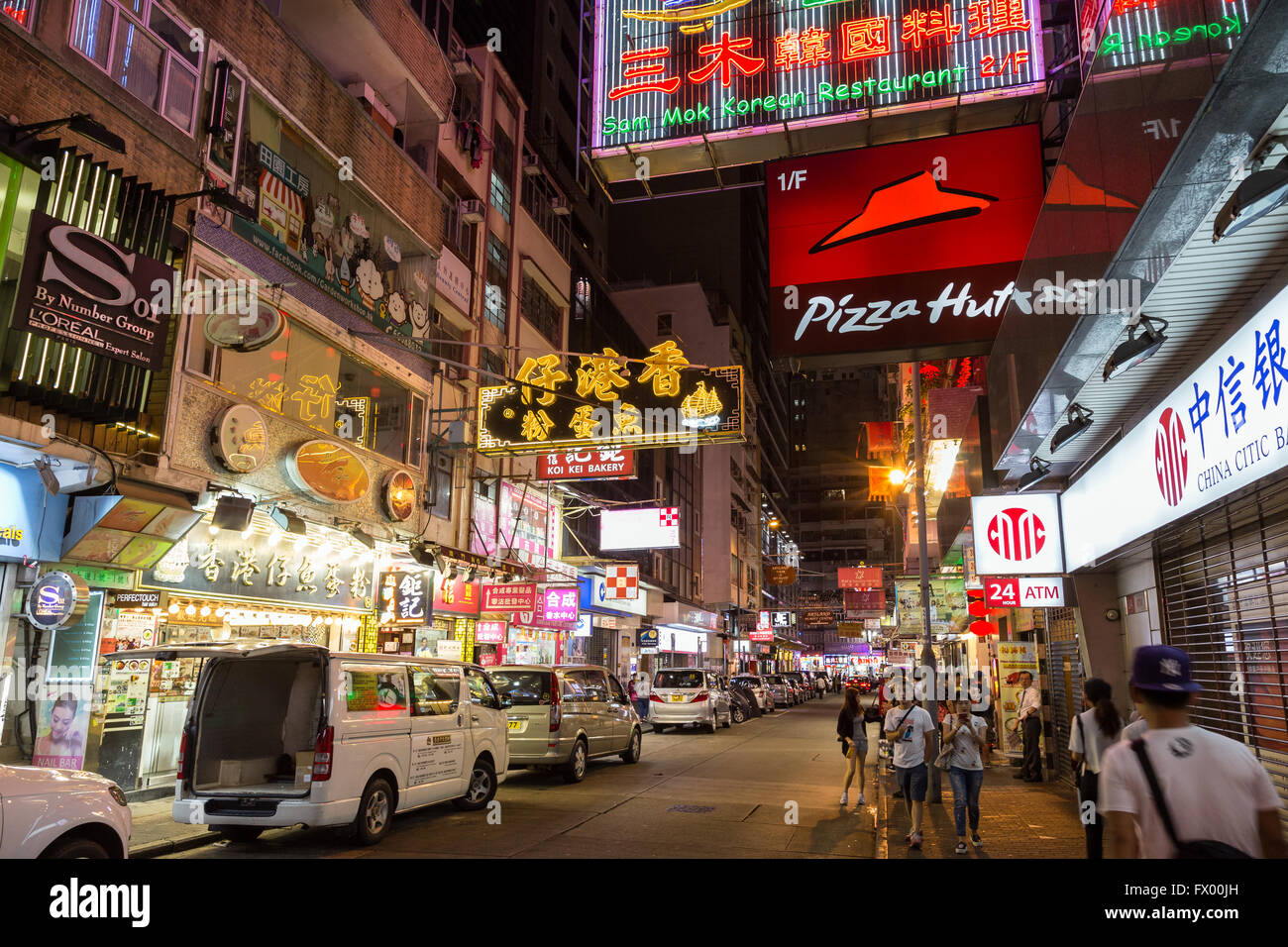 Menschen und Autos auf einer Straße voller Geschäfte und Restaurants in Tsim Sha Tsui, Hongkong, China, in der Nacht. Stockfoto