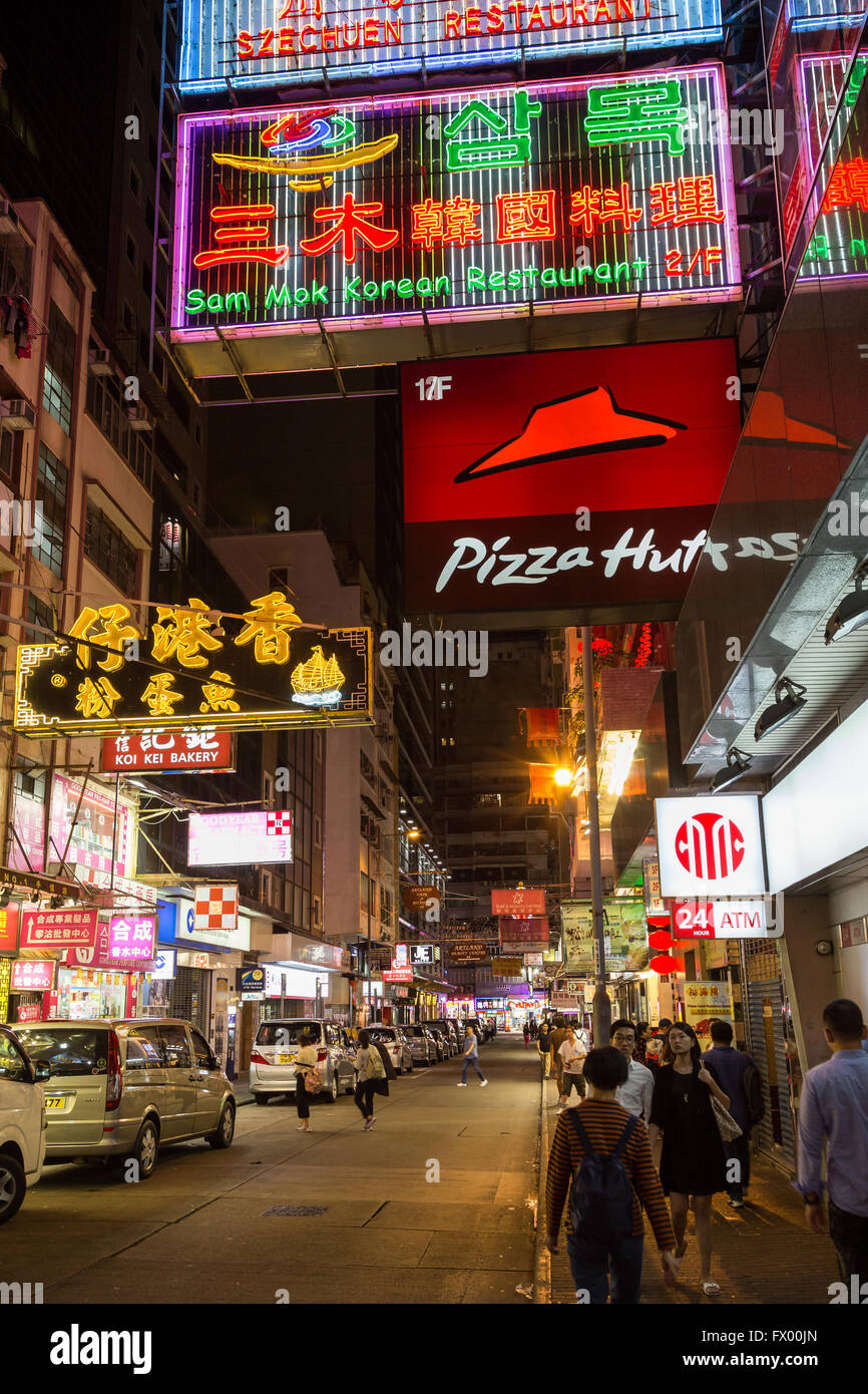 Menschen und Autos auf einer Straße voller Geschäfte und Restaurants in Tsim Sha Tsui, Hongkong, China, in der Nacht. Stockfoto